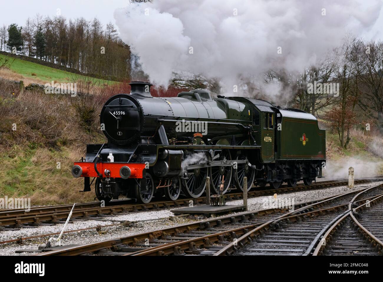 Historic steam train (green shiny loco) stationary on track, puffing smoke clouds on scenic rural heritage railway - KWVR, Yorkshire, England, UK. Stock Photo