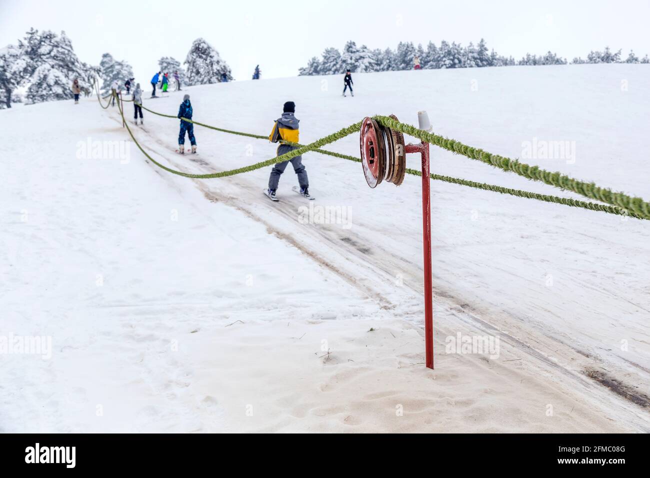 Drive wheel of a homemade ski lift with teenage skiers in background at