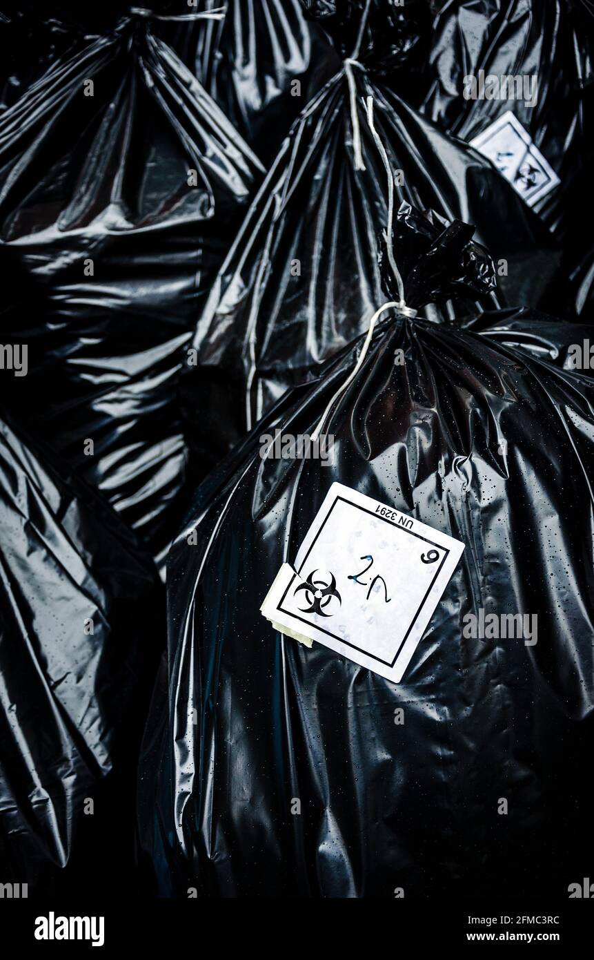 Biohazard waste disposable black bags with logo on stickers, hospital waste on street in a rainy day Stock Photo