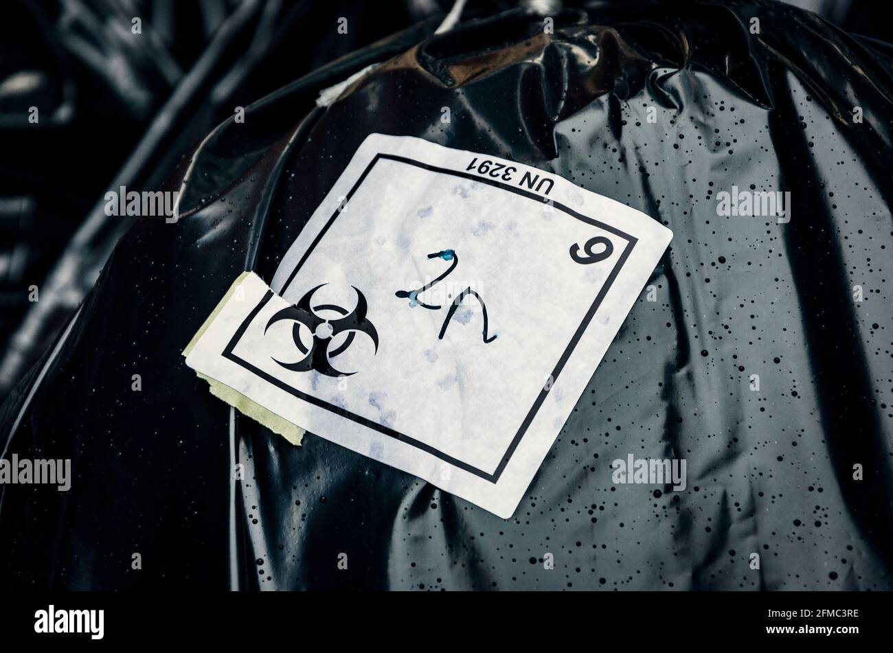 Biohazard waste disposable black bags with logo on sticker, hospital waste on street in a rainy day Stock Photo