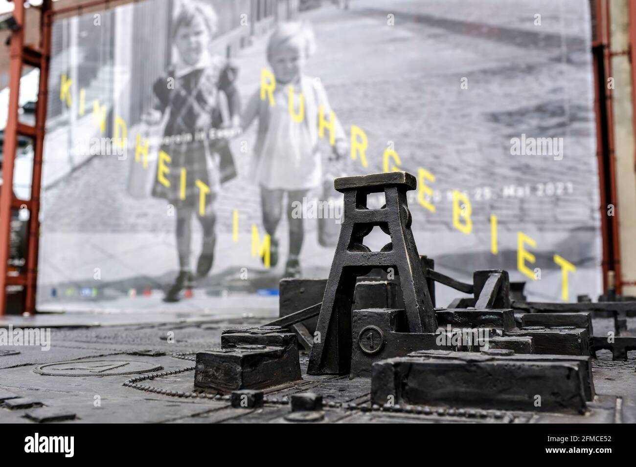 07.05.2021, Essen, Nordrhein-Westfalen, Deutschland - Blick ueber ein kleines Modell der Zeche Zollverein aus Eisen auf ein Werbeplakat fuer die Ausst Stock Photo