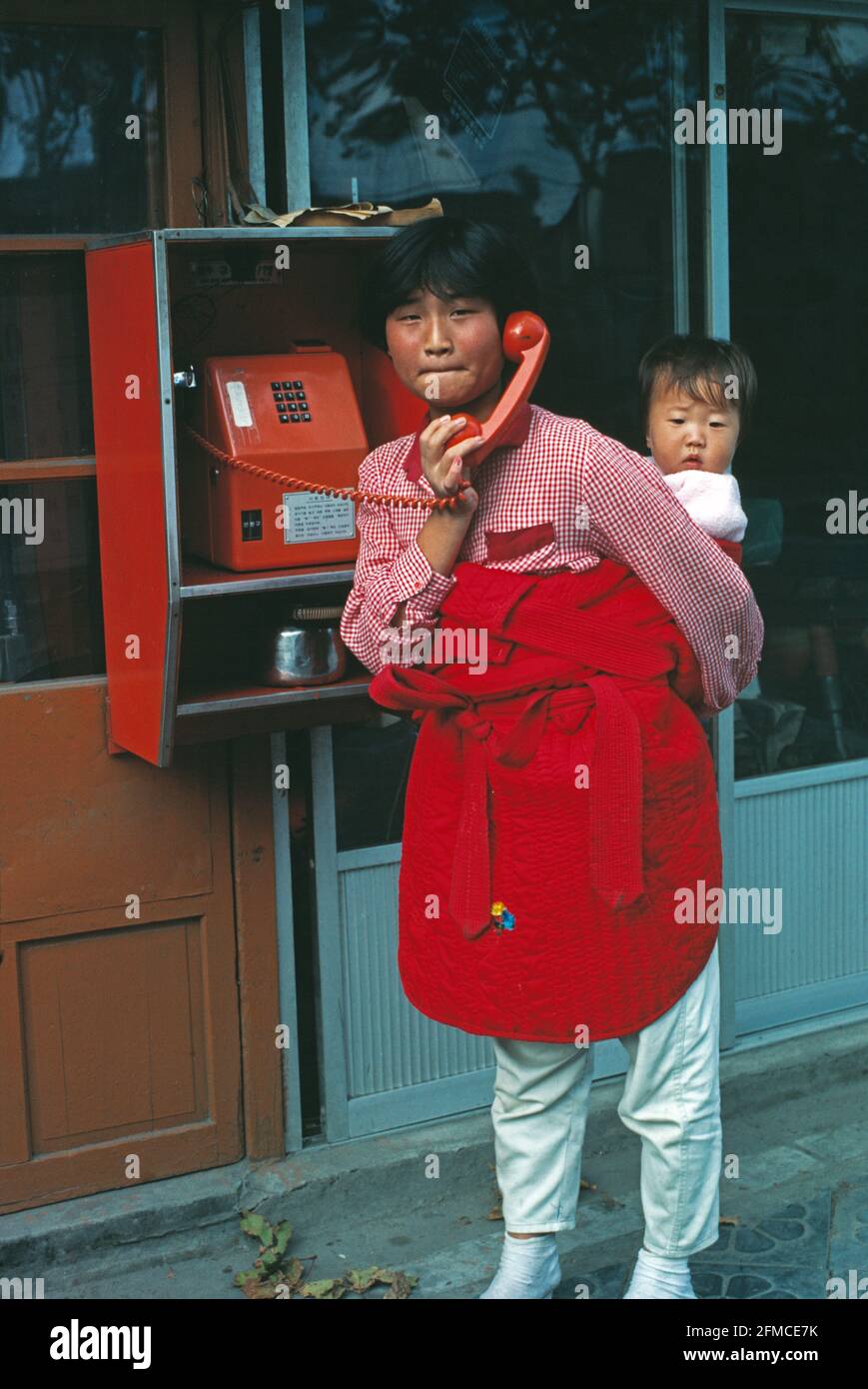 South Korea. Seoul city. Woman using public telephone. Child on her back. Stock Photo