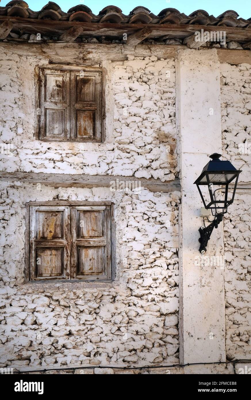 An old and run-down house with a street lamp on the whitewashed stone wall in Libros, near Teruel, Aragon, Spain. Weathered wooden shutters are closed Stock Photo