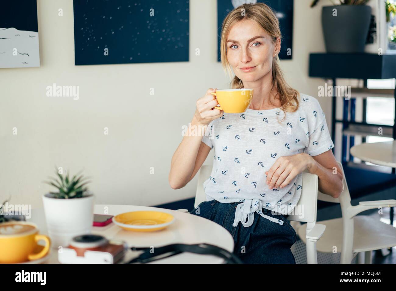 Young caucasian stylish smiling blonde is drinking coffee in a coffee shop. Stock Photo
