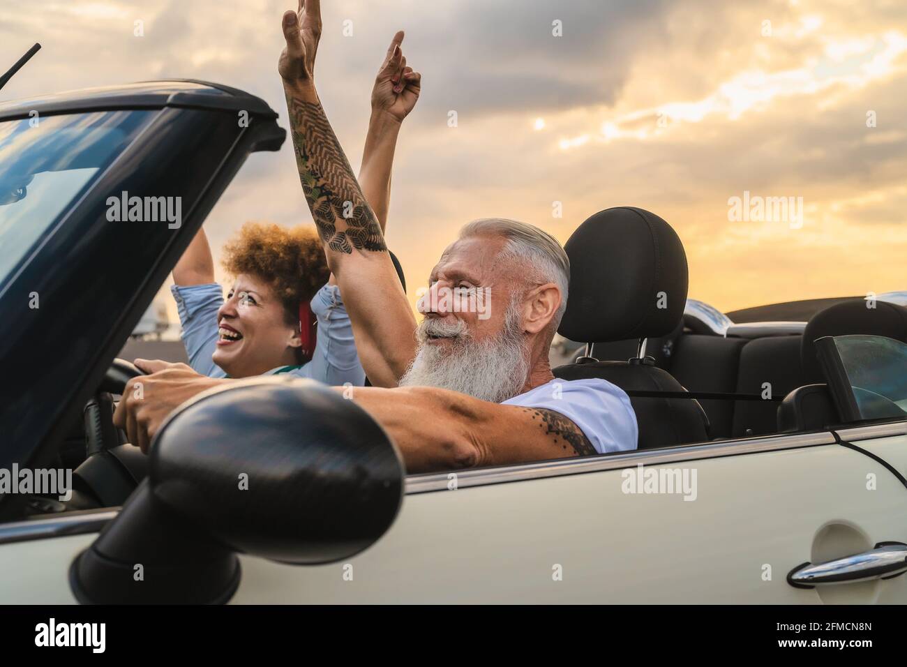 Happy senior couple having fun driving on new convertible car - Mature people enjoying time together during road trip tour vacation Stock Photo