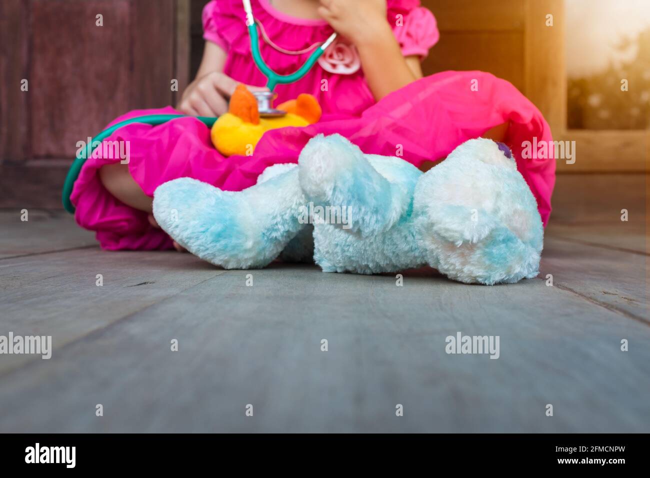 Child playing doctor or nurse with plush toy duck with bright sunlight at home. Happy girl listens a stethoscope to toy. Playful girl role playing. Stock Photo