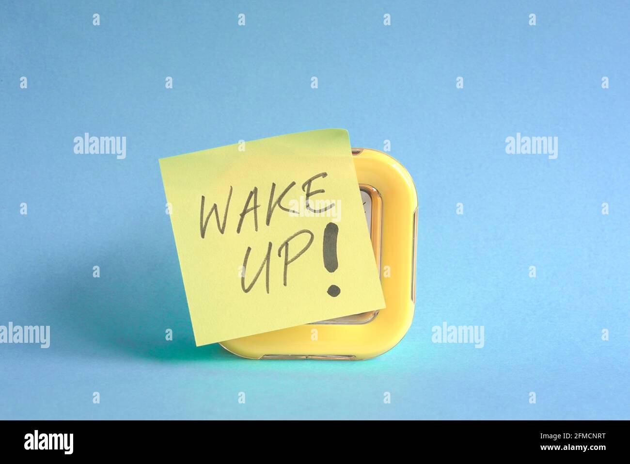 Wake up message written on marker pen stick on yellow clock. On blue background. Stock Photo