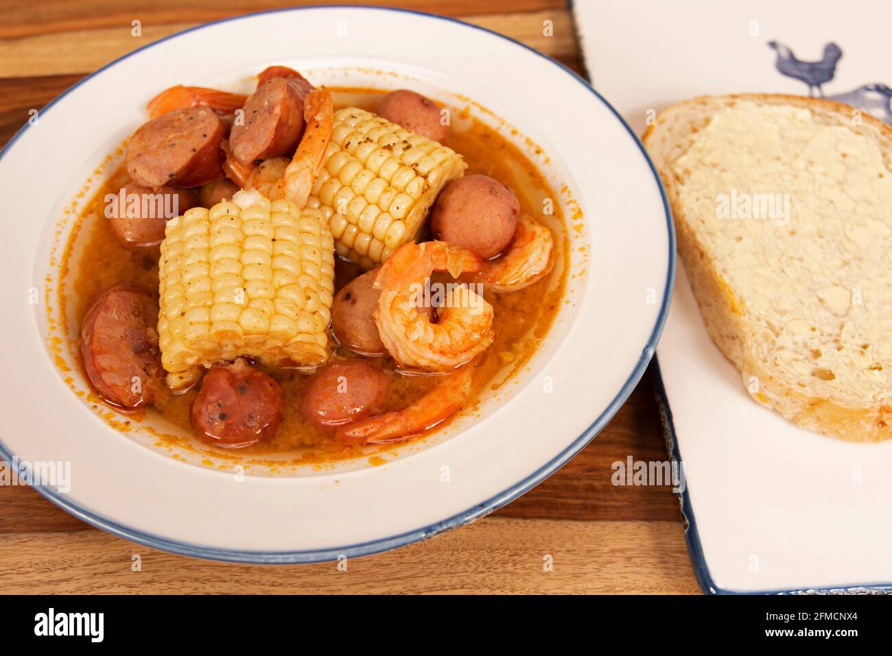 Homemade Cajun Shrimp Boil with corn, new potatoes, and andouille sausage with a slice of sourdough bread, served in a white bowl Stock Photo