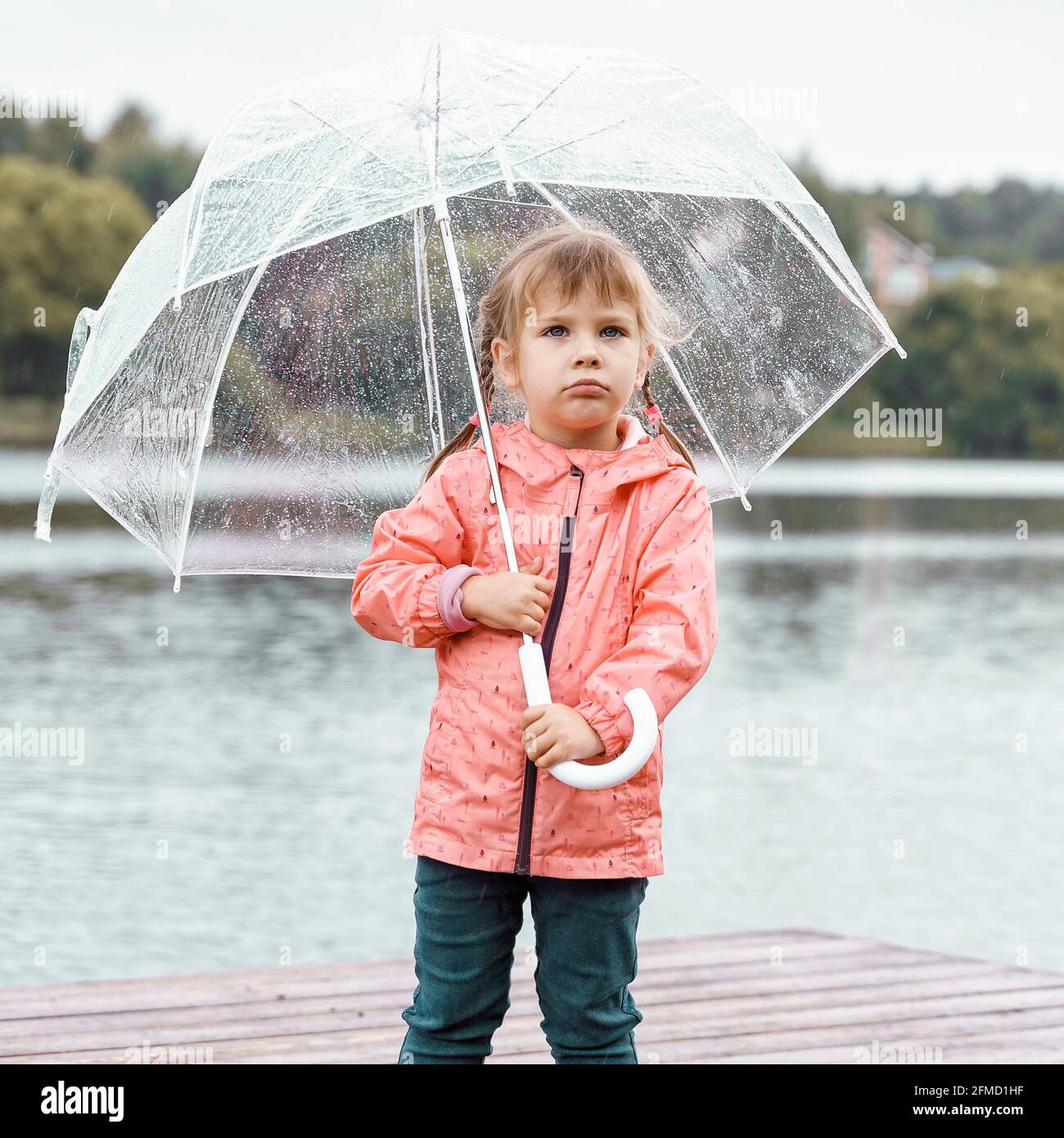 sad little girl with umbrella in the rain by the pond. rainy ...