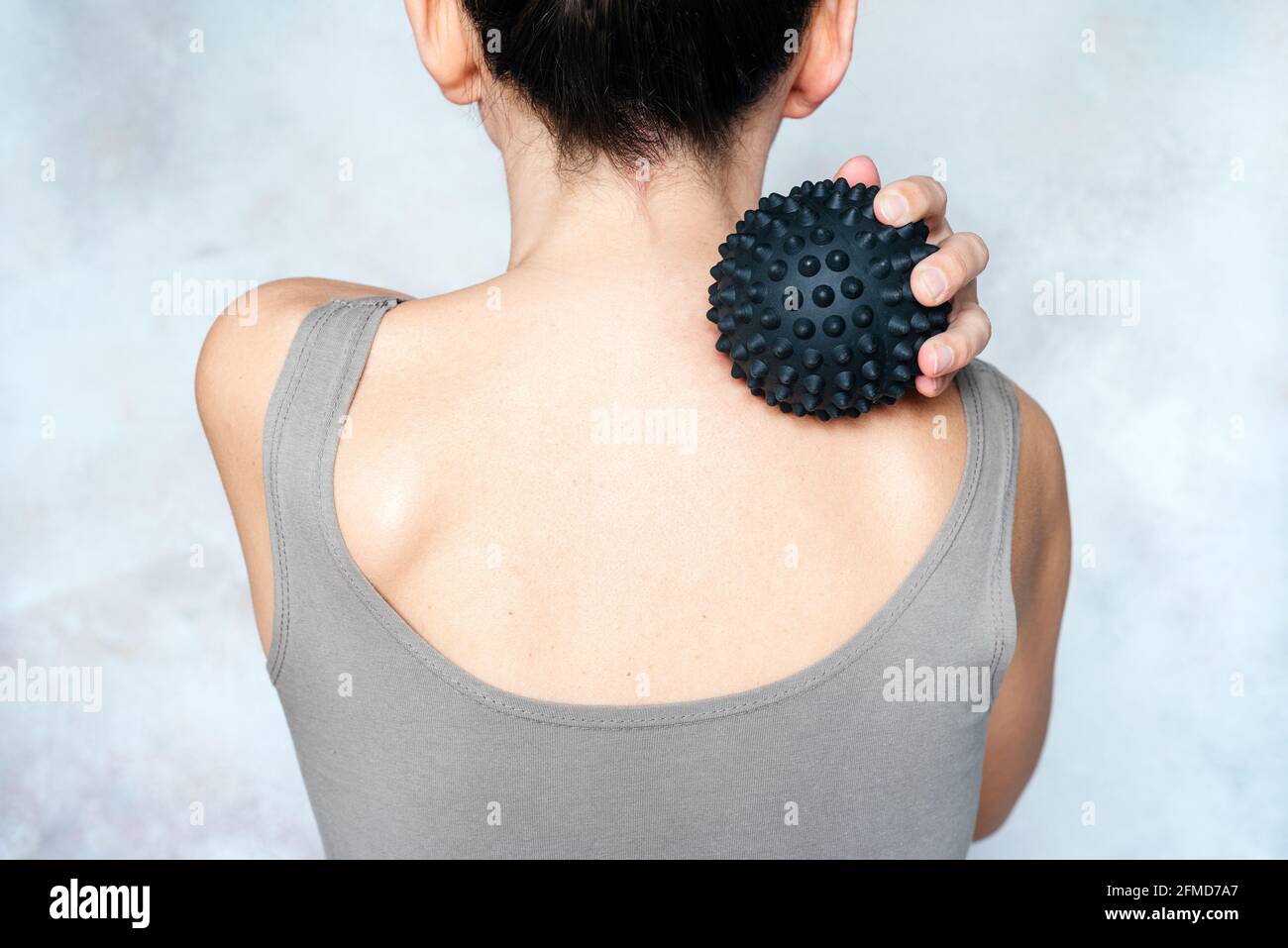 Young woman massages her back with spiky trigger point ball, muscle pain treatment reflexology