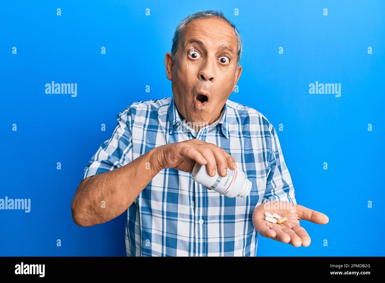 Senior hispanic man holding pills afraid and shocked with surprise and