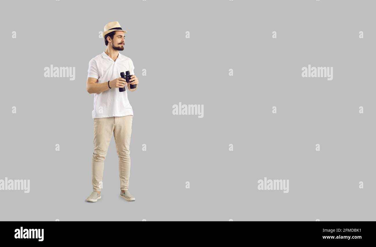 Young man in casual outfit holding binoculars standing on grey copy space background Stock Photo