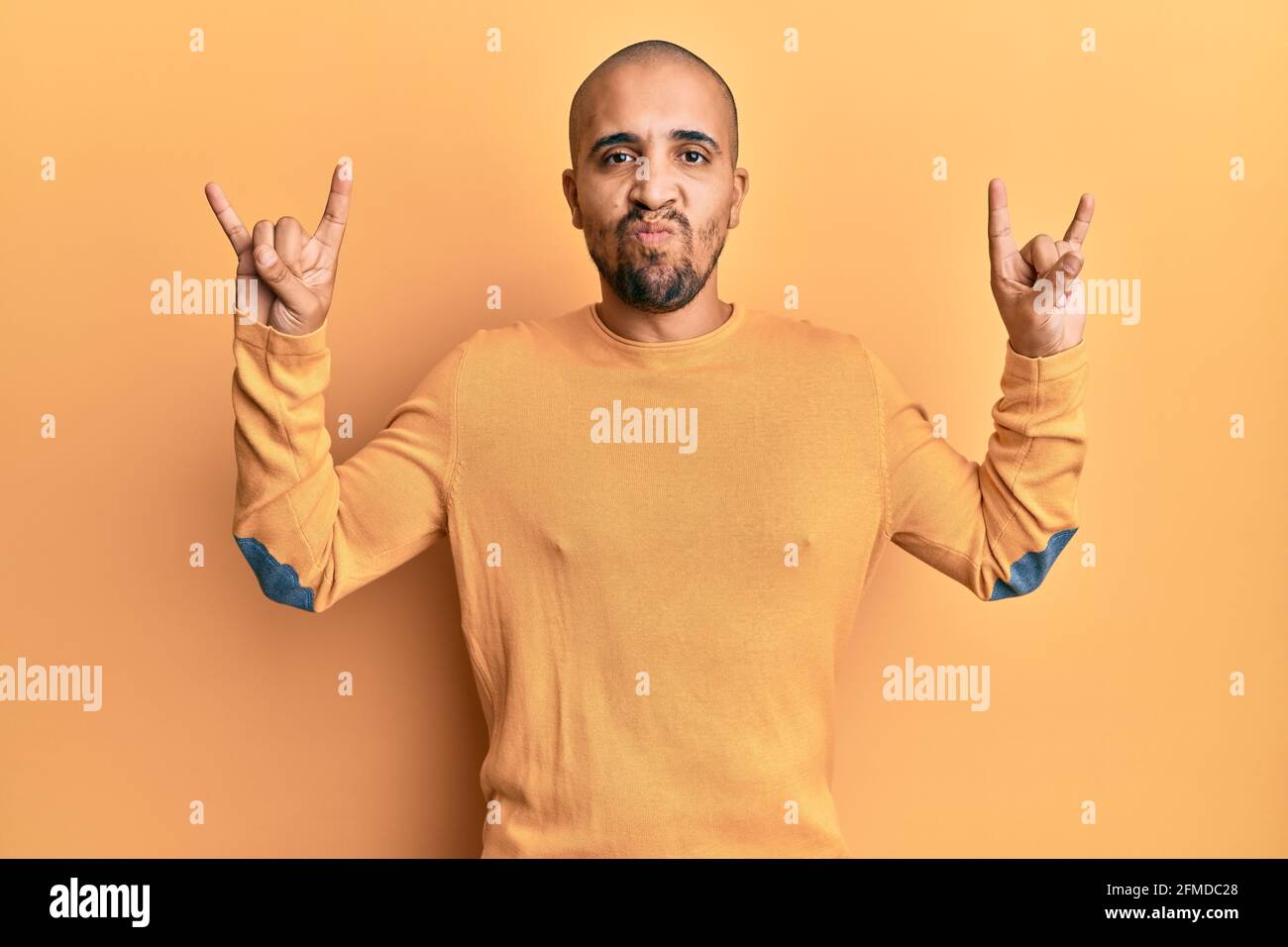 Hispanic adult man doing rock gesture over yellow background skeptic ...