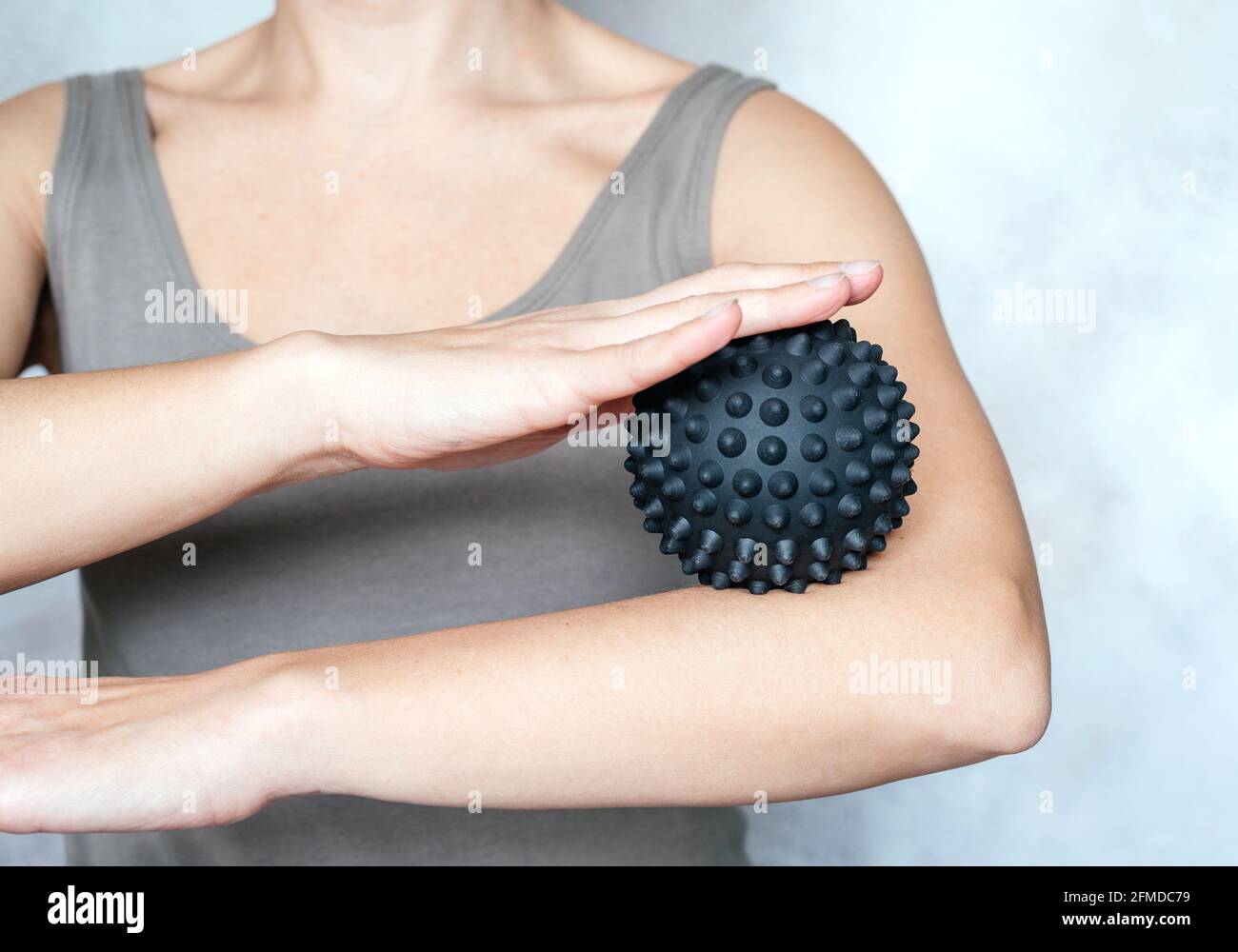A young woman massages her elbow with spiky trigger point ball, tennis