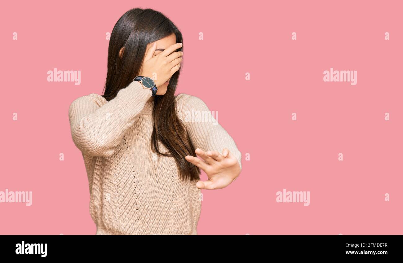 Young brunette woman wearing casual winter sweater covering eyes with hands and doing stop gesture with sad and fear expression. embarrassed and negat Stock Photo