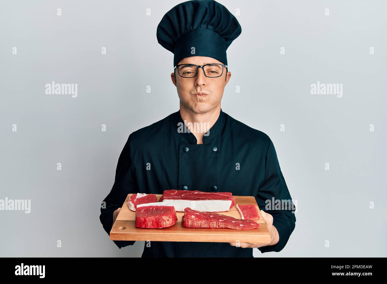 Handsome young man wearing chef uniform holding board with raw meat