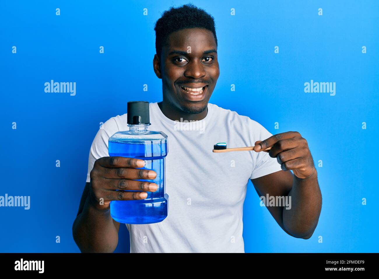 Handsome black man holding mouthwash and toothbrush for fresh breath