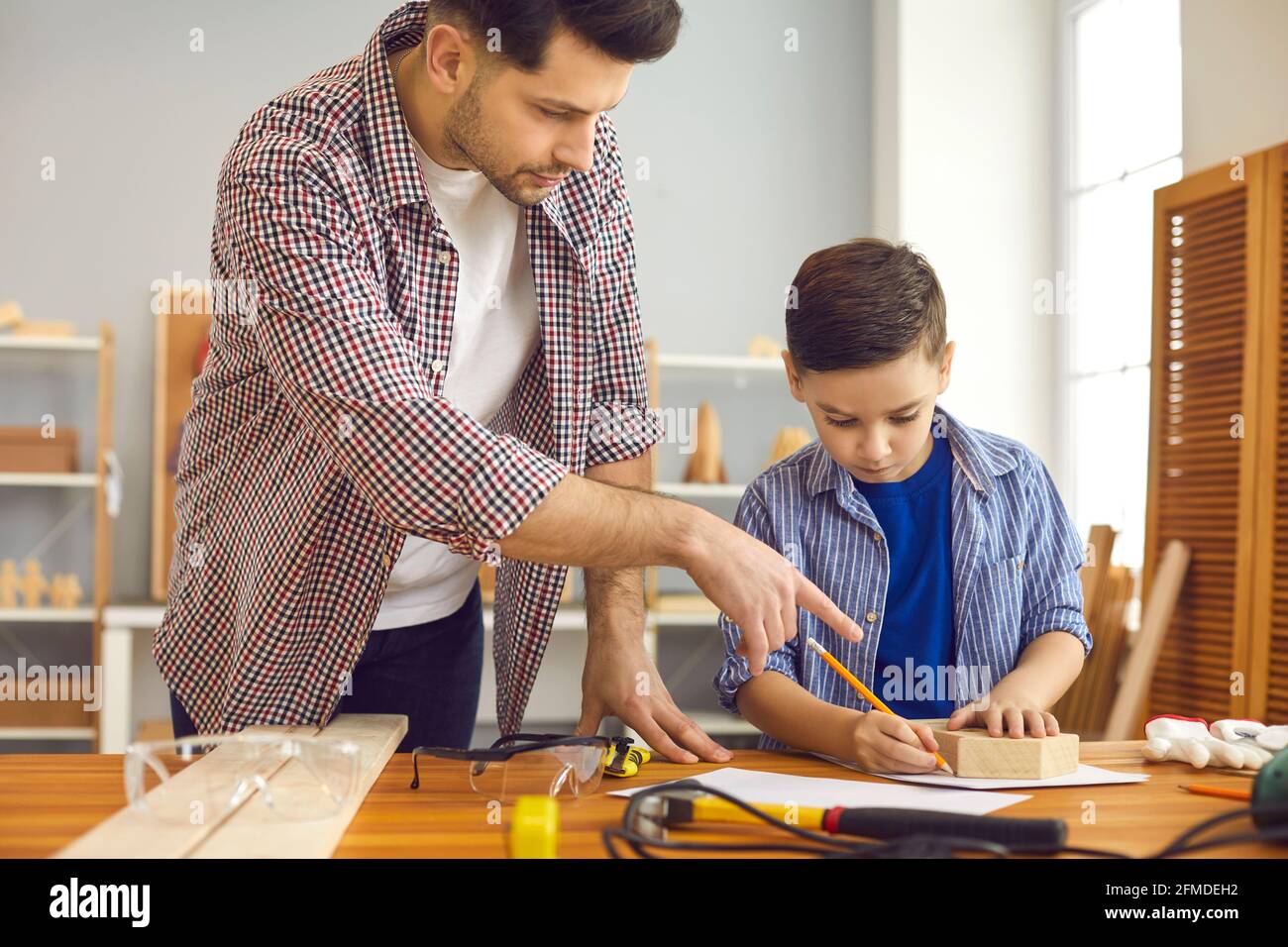 Father teaching son to build toy house at home carpentry and joinery workshop Stock Photo