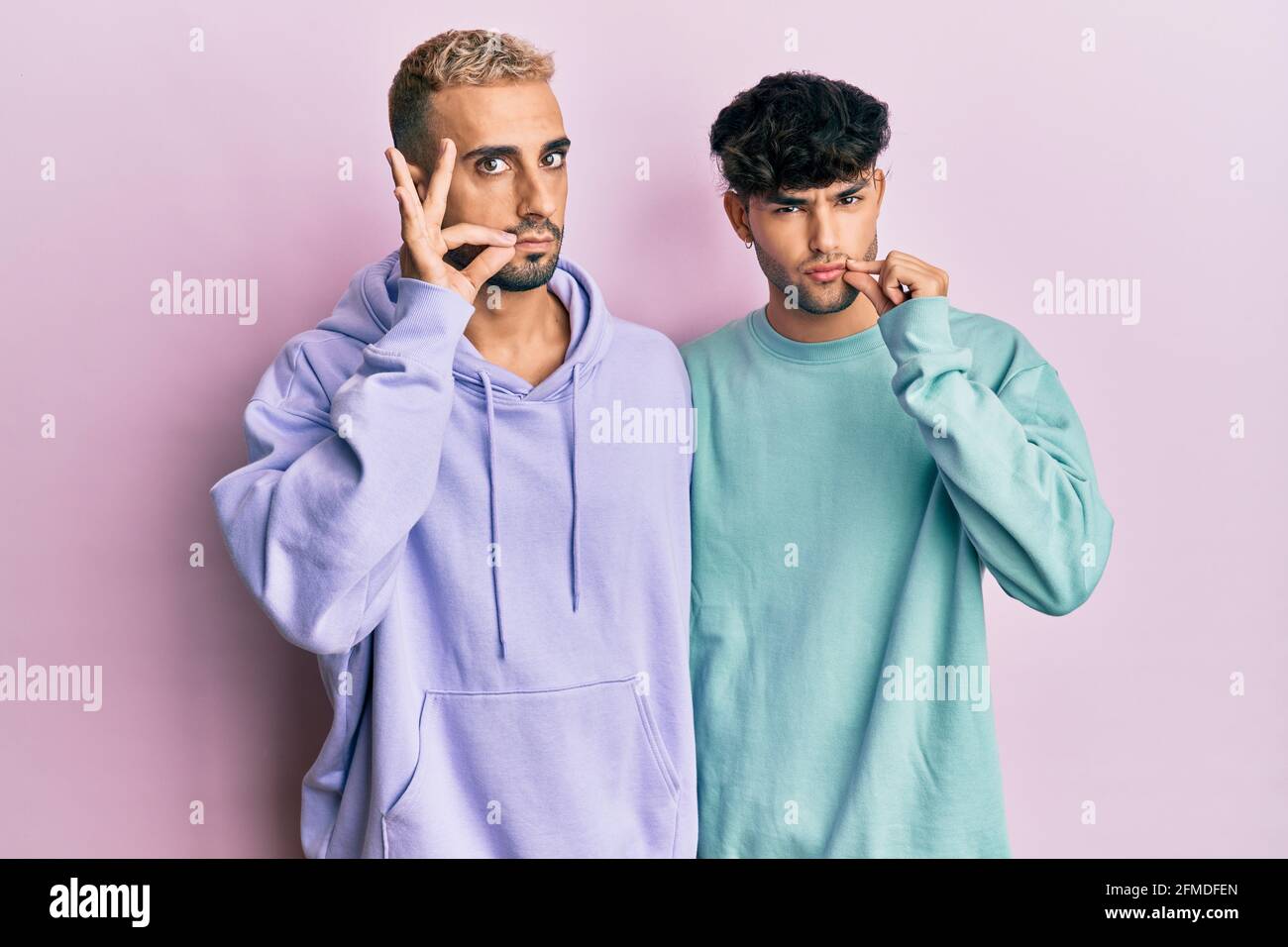 Homosexual gay couple standing together wearing casual clothes mouth and  lips shut as zip with fingers. secret and silent, taboo talking Stock Photo  - Alamy