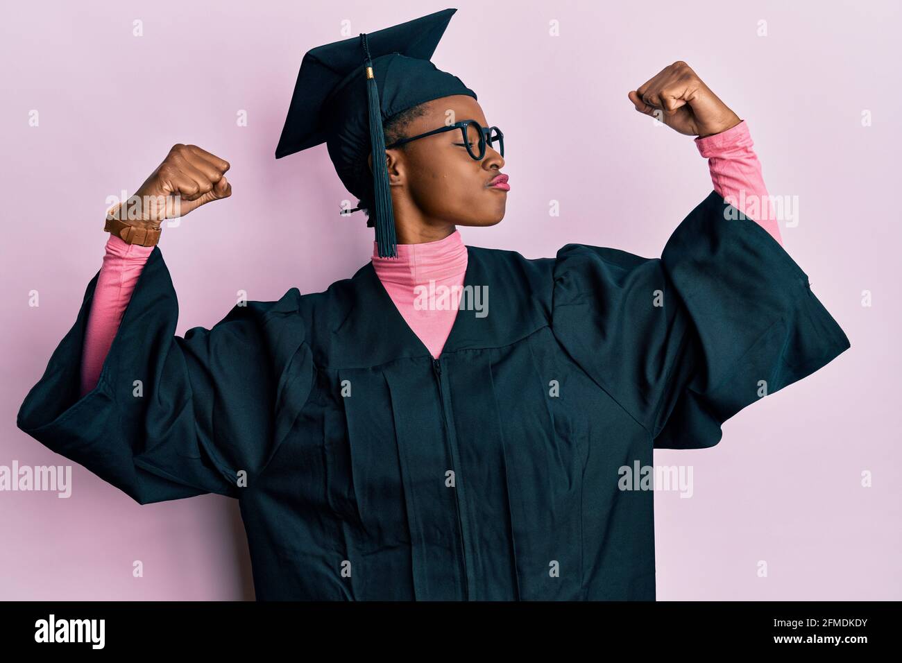 Young african american girl wearing graduation cap and ceremony robe showing arms muscles smiling proud. fitness concept. Stock Photo