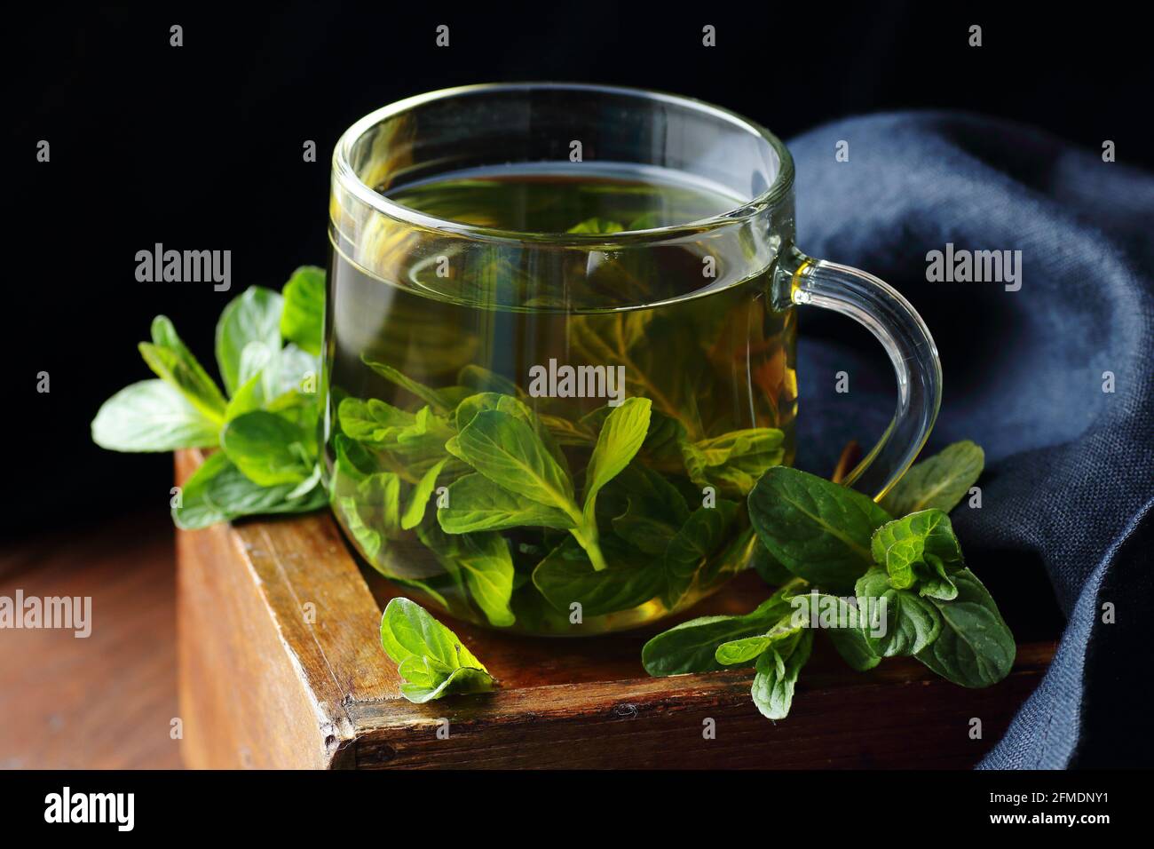 Mint herbal tea in a glass cup on dark moody wooden rustic background with blue linen napkin, closeup, copy space, natural medicine, naturopathy, drin Stock Photo