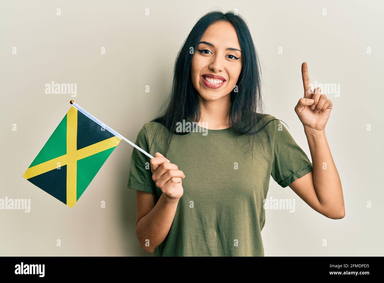 Young hispanic girl holding jamaica flag smiling with an idea or question  pointing finger with happy face, number one Stock Photo - Alamy
