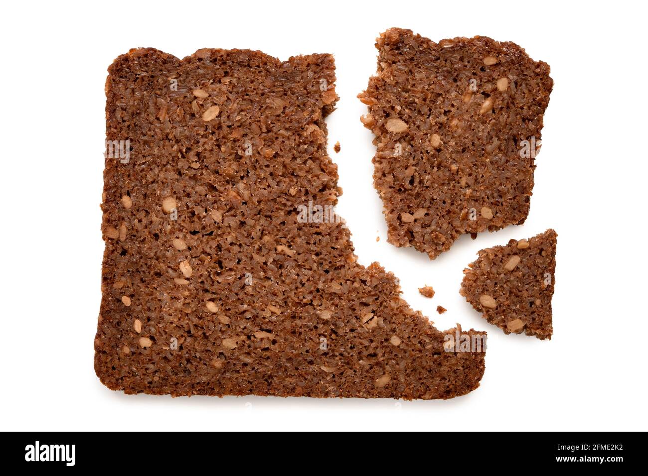 Broken slice of German health bread with sunflower seeds isolated on white. Top view. Stock Photo