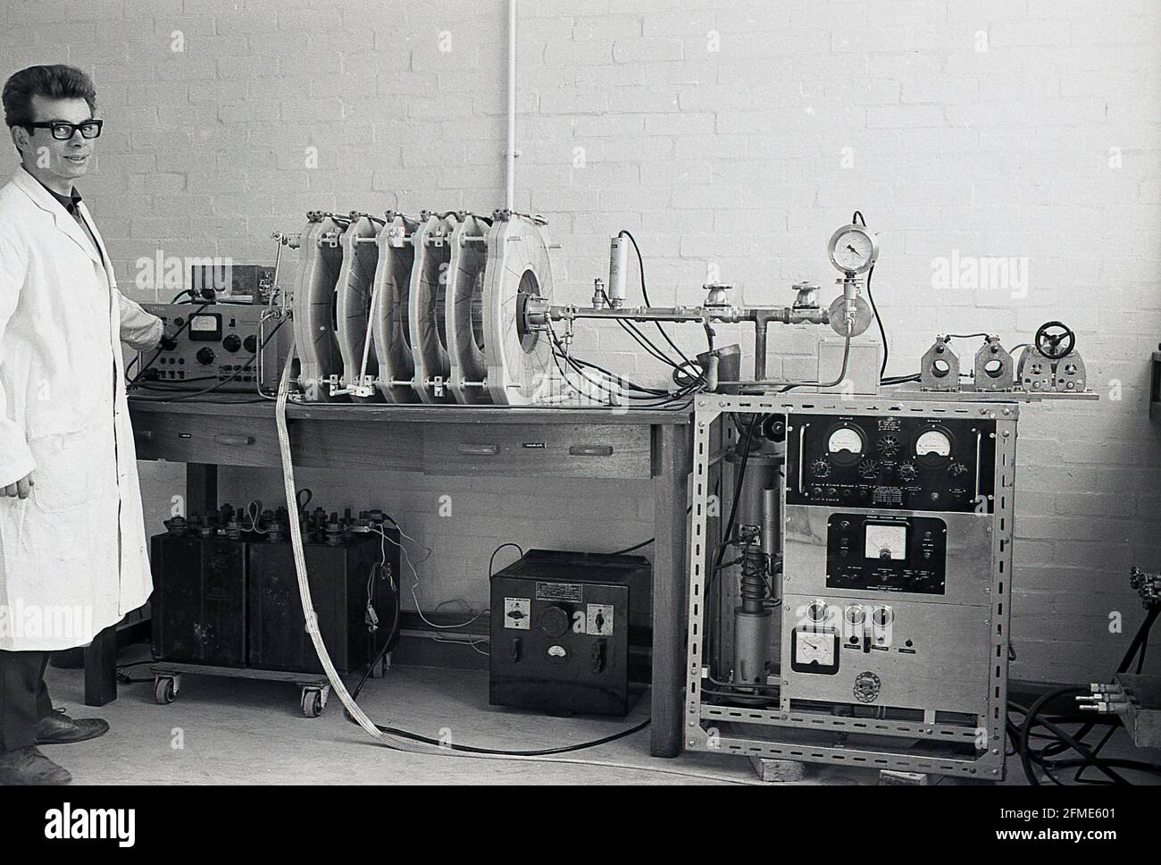 1963, historical, a white-coated male technician standing beside equipment being tested by an oscilloscope, often known simply as a scope or o-scope, a type of electronic test instrument that graphically displays signal voltages and measures voltage waves. Stock Photo