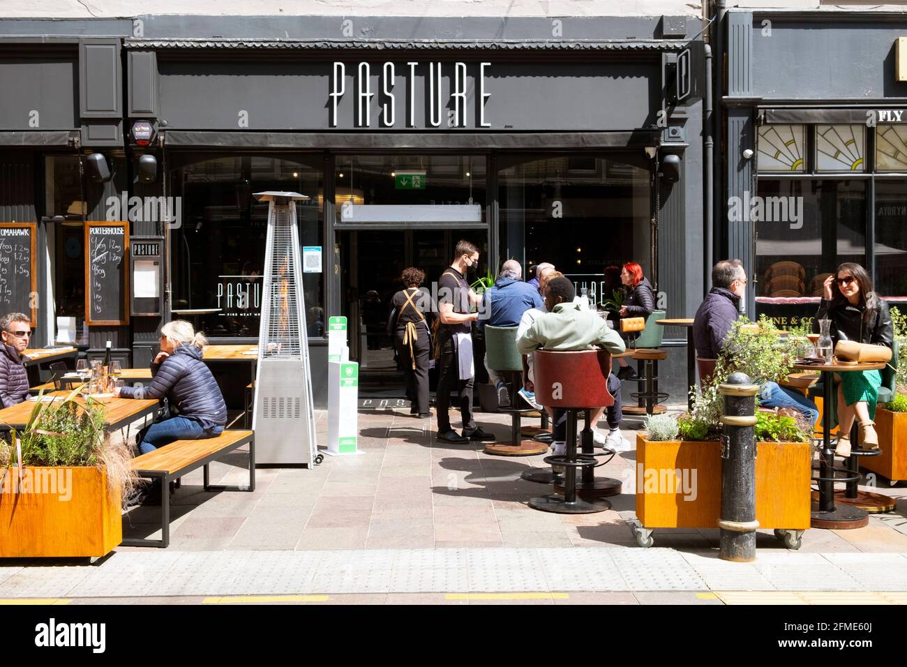 View of waiter wearing face mask people sitting outside PASTURE restaurant in St Mary Street after lockdown Cardiff City Centre May 2021 KATHY DEWITT Stock Photo