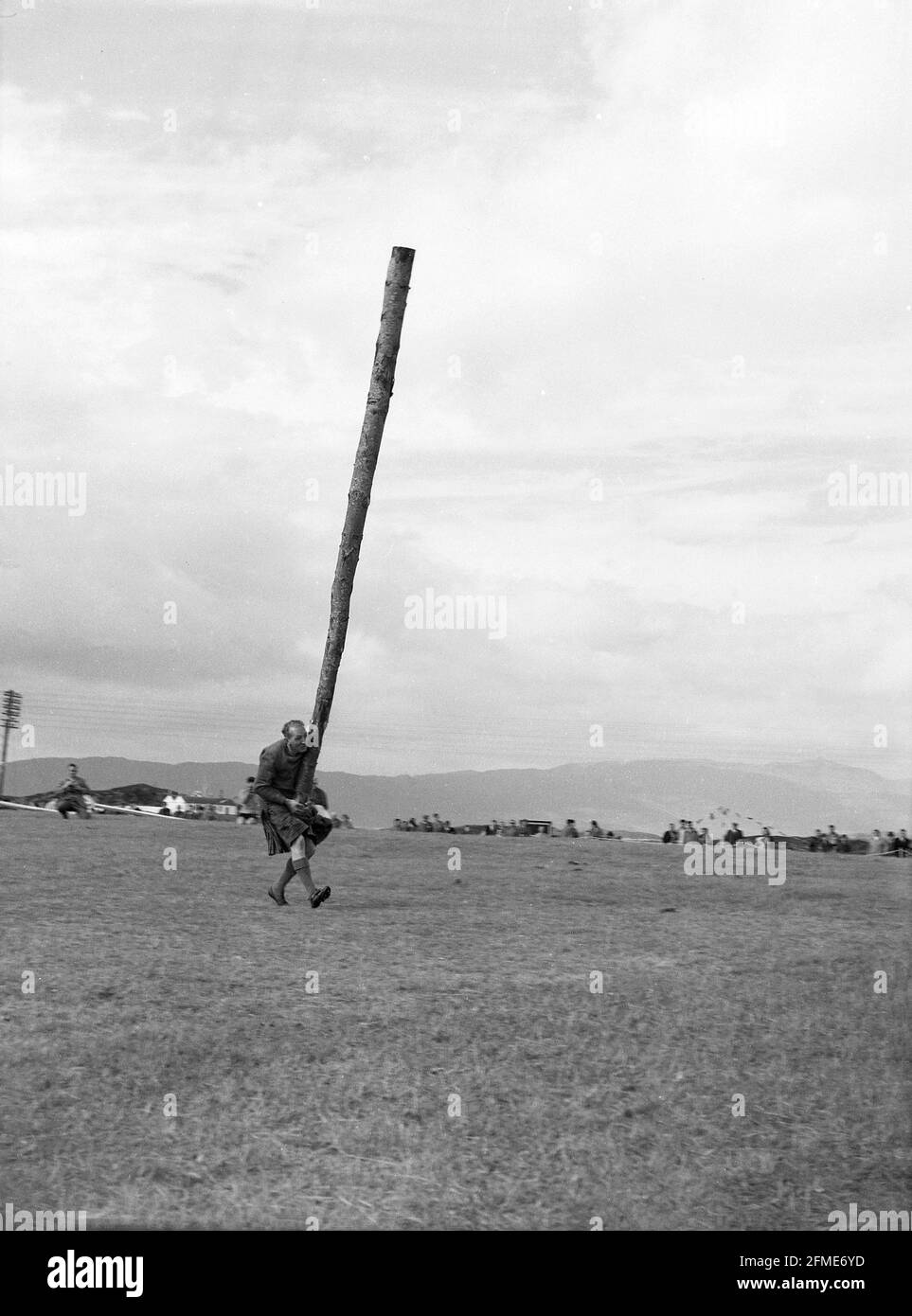 1956, a competitor at a highland games about to toss the caber, Scotland, UK. A traditional and well-loved athletic event at a Scottish highland games, the 'caber toss' involves a competitor tossing a long, heavy pole so that it turns end over end. Usually made from a Larch tree, and up to 20 feet in length, the caber is stood upright and then lifted up and tossed, not thrown. Caber is the Gaelic word for pole. Devised by Scottish woodsmen, the caber toss was first recorded in 1574, at a military meet  as toss 'ye barr', when clan warriors tested their physical strength in sporting contests. Stock Photo