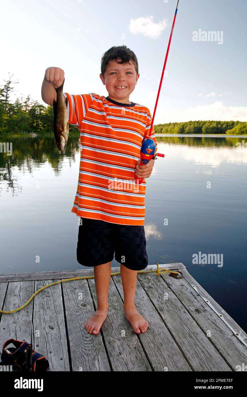 A 7 yr old boy fishing from a wharf and holding a fish Stock Photo