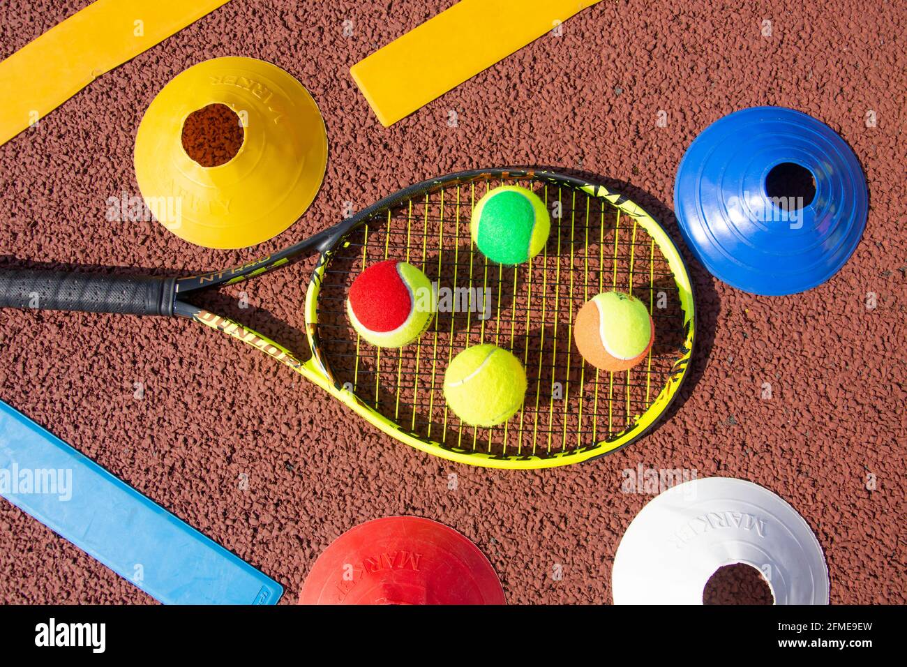 Selection of red, green, orange and yellow tennis balls on tennis racket with lay-downs and cones, Surrey, England, United Kingdom Stock Photo