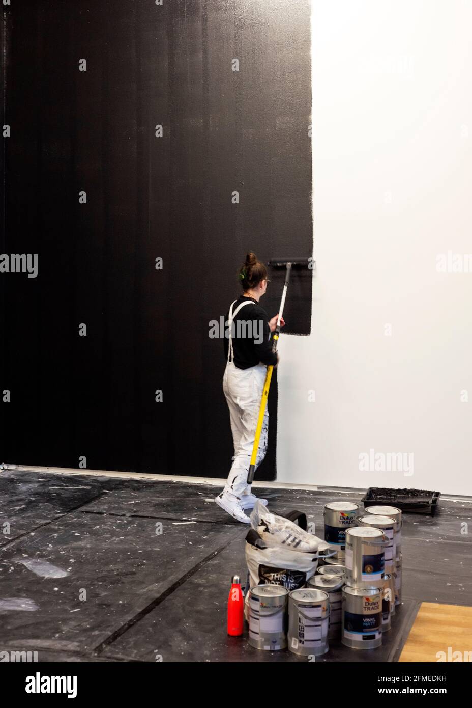Young woman artist worker painting walls in black and white as part of performance art work installation called A Life ( Black and White) by Bulgarian artist Nedko Solakov in Tate Modern, London, United Kingdom as of February 2020. Stock Photo