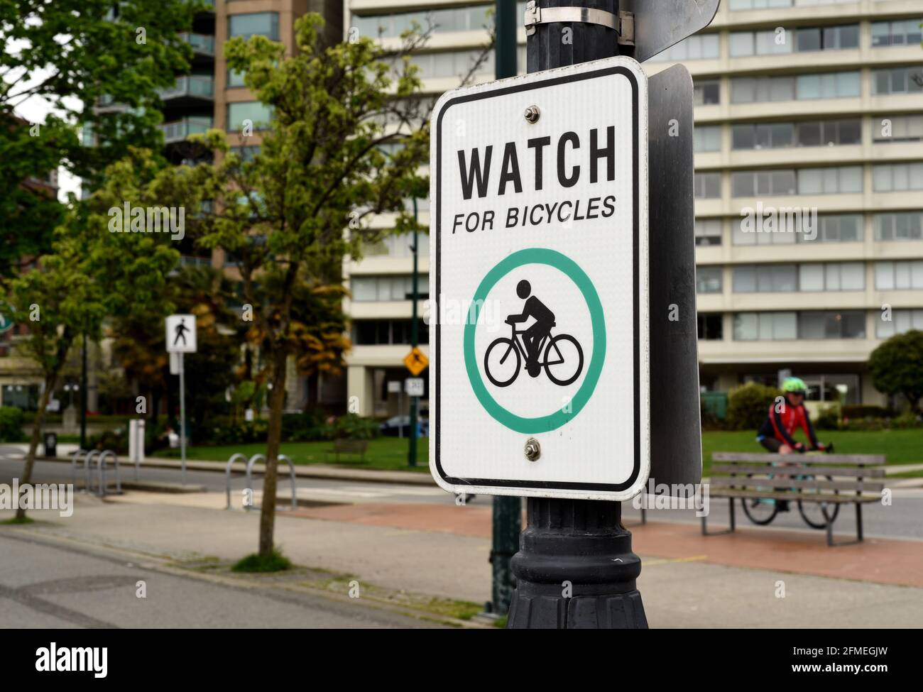 A cyclist pedals past a sign warning pedestrians to Watch For Bicycles along English Bay in the West End in Vancouver, British Columbia, Canada Stock Photo