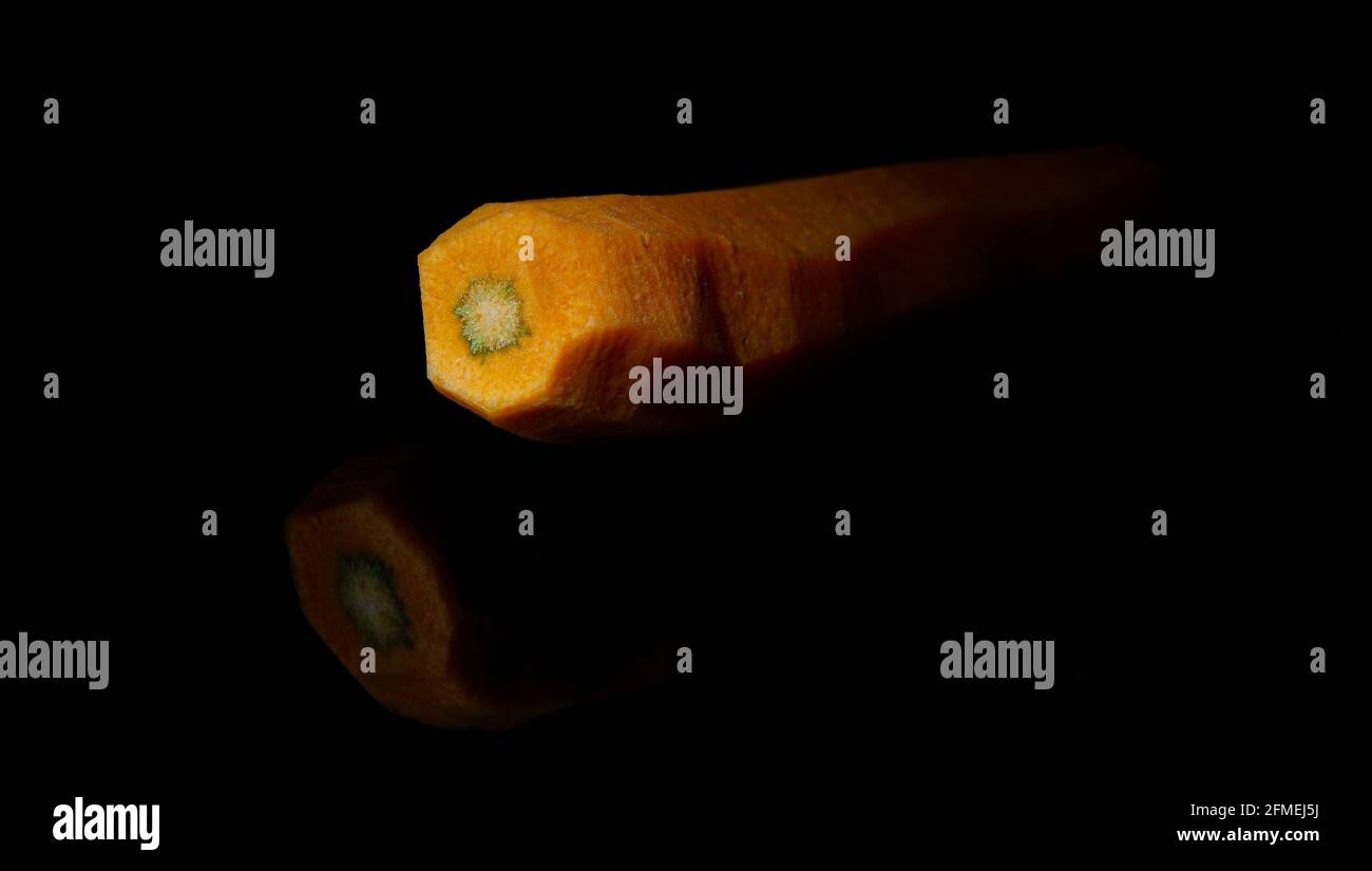 One carrot, the surface structure in a close-up view. The vegetable cross-section. Food still life on a glossy smooth black background with object mir Stock Photo