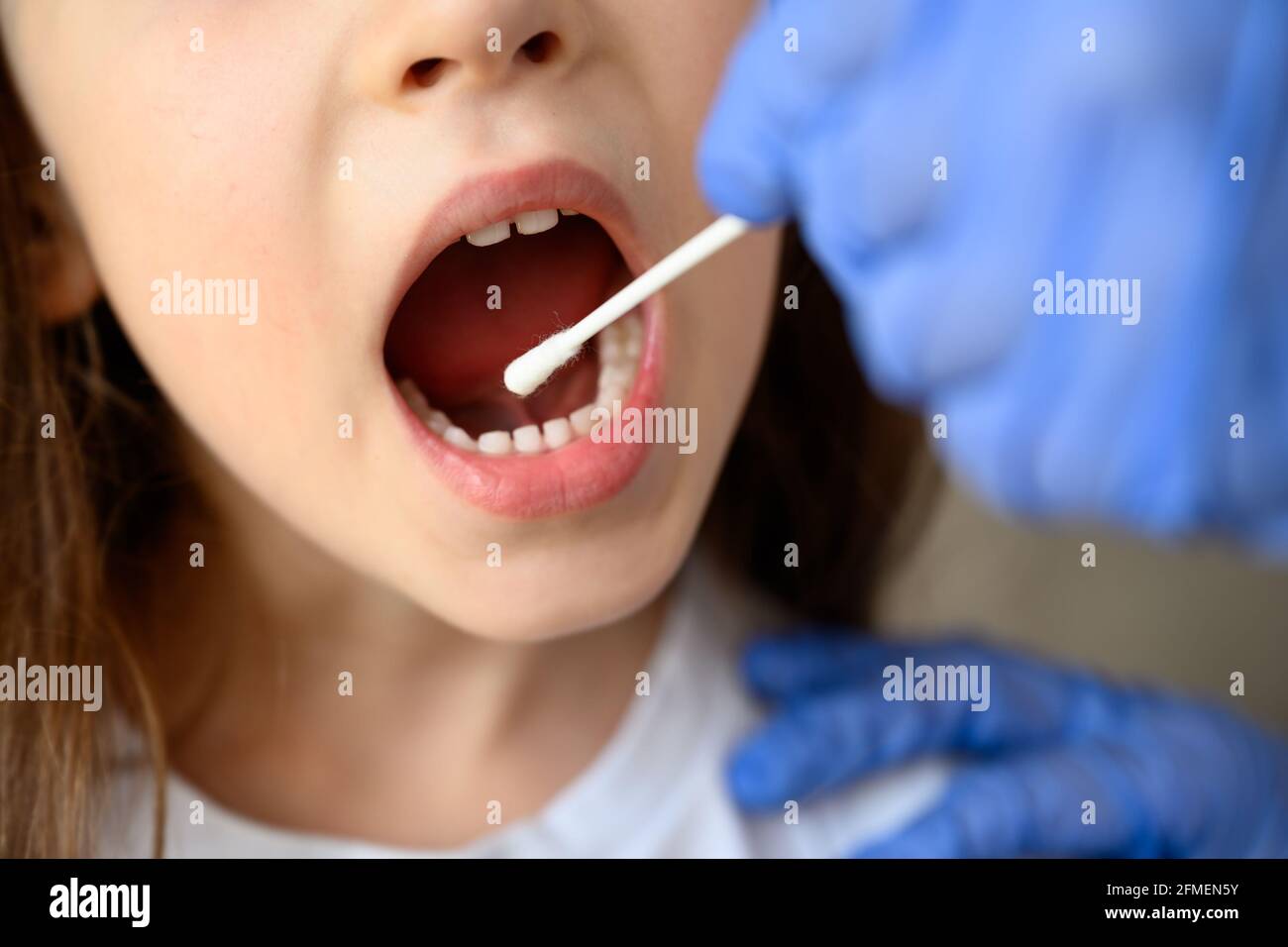 Coronavirus test and mouth, kid opens mouth for COVID-19 diagnostics. Doctor or nurse holds swab for saliva sample from child. Corona virus oral PCR t Stock Photo