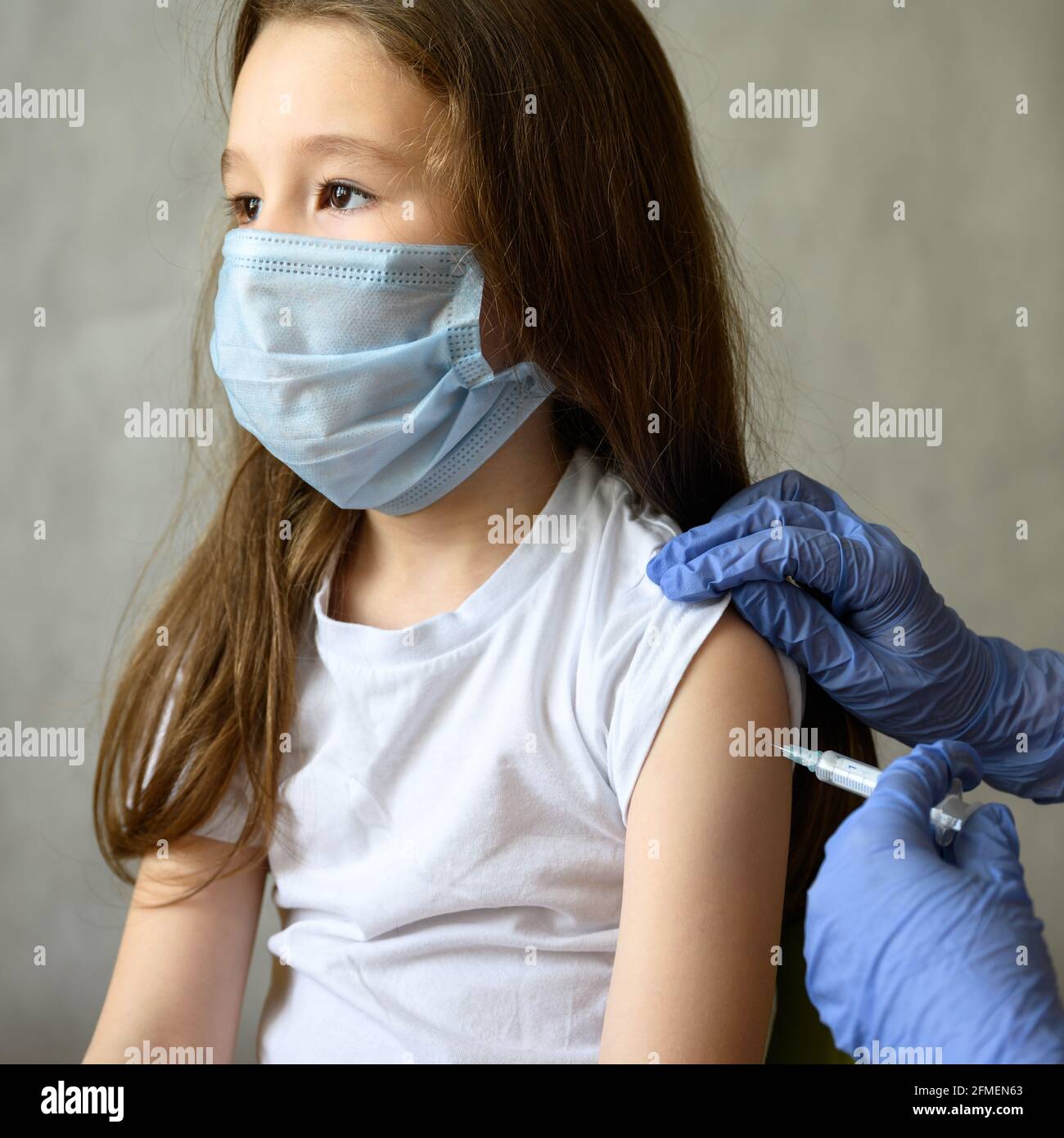 Vaccination of cute child from COVID-19 or flu, pretty little girl during coronavirus vaccine injection. Portrait of adorable kid with mask and syring Stock Photo