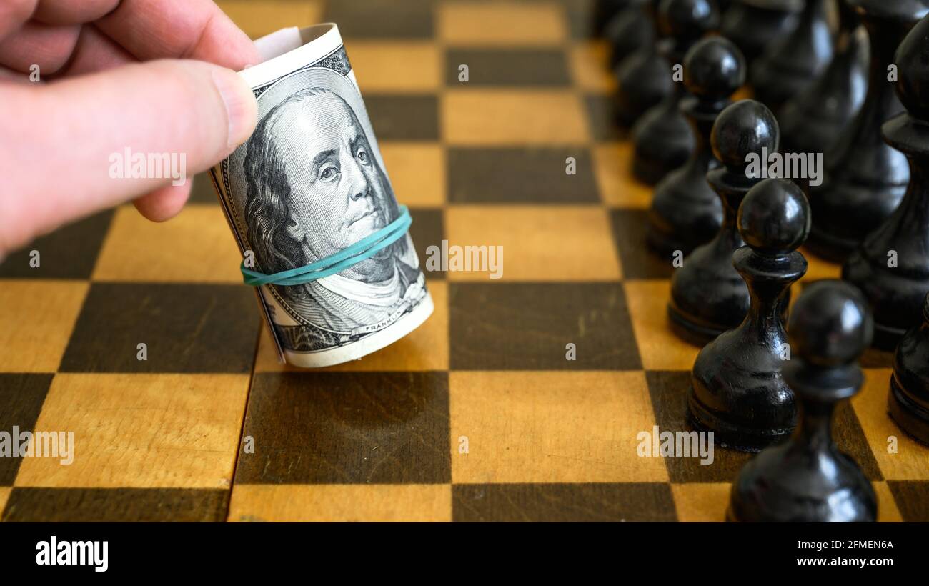 Chess game and rolled dollar bills as white move, US money on chessboard. American banknotes and chess figures. Concept of business strategy, dollar l Stock Photo