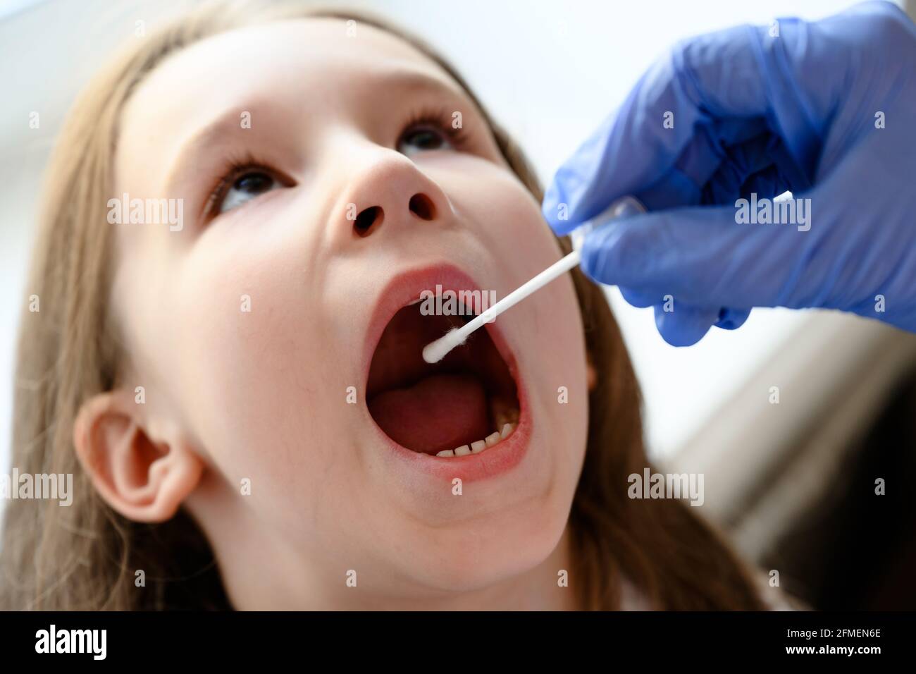 Kid opens mouth for COVID-19 test, doctor holds swab for saliva sample from cute child during coronavirus pandemic. Nurse hand and little girl face cl Stock Photo