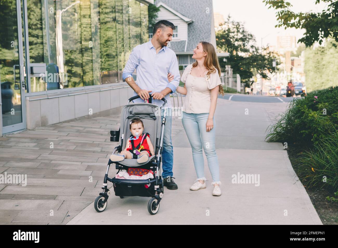 Caucasian mother and father walking with baby daughter in stroller. Family  strolling together outdoors on city street on summer day. Urban life with k  Stock Photo - Alamy