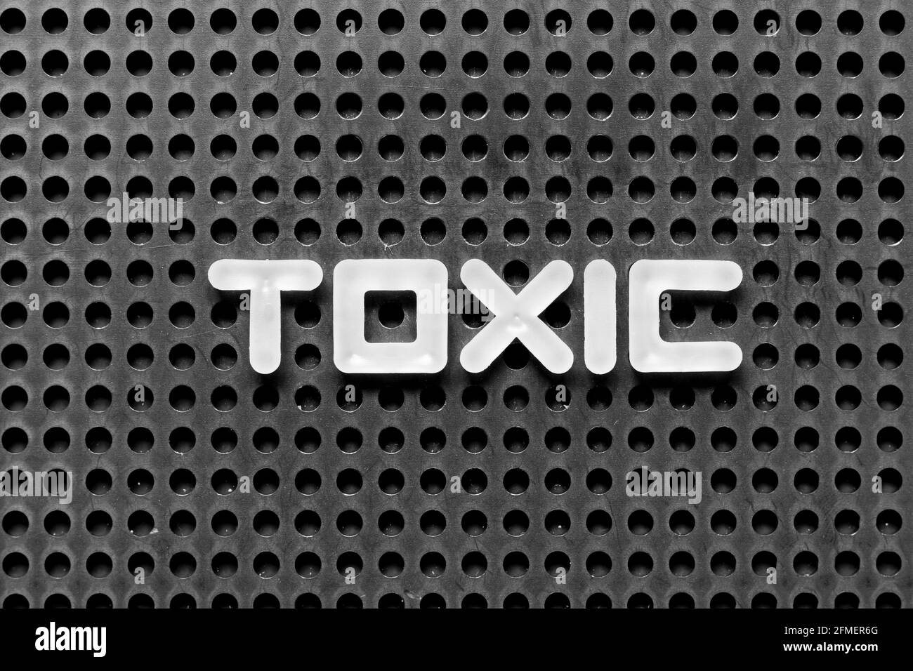 White alphabet letter in word toxic on black pegboard background Stock Photo