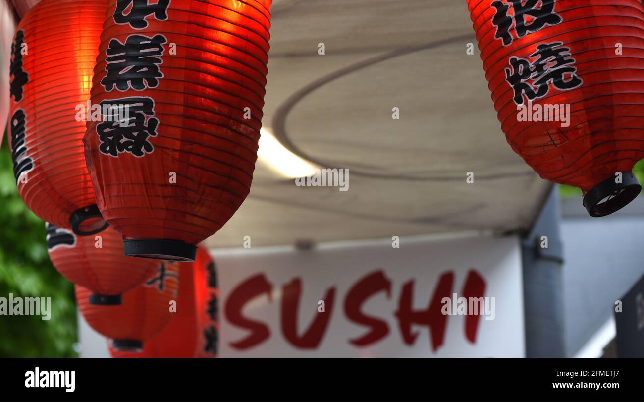 Asian paper lanterns with text glow next to a sign for sushi at a restaurant in the West End in