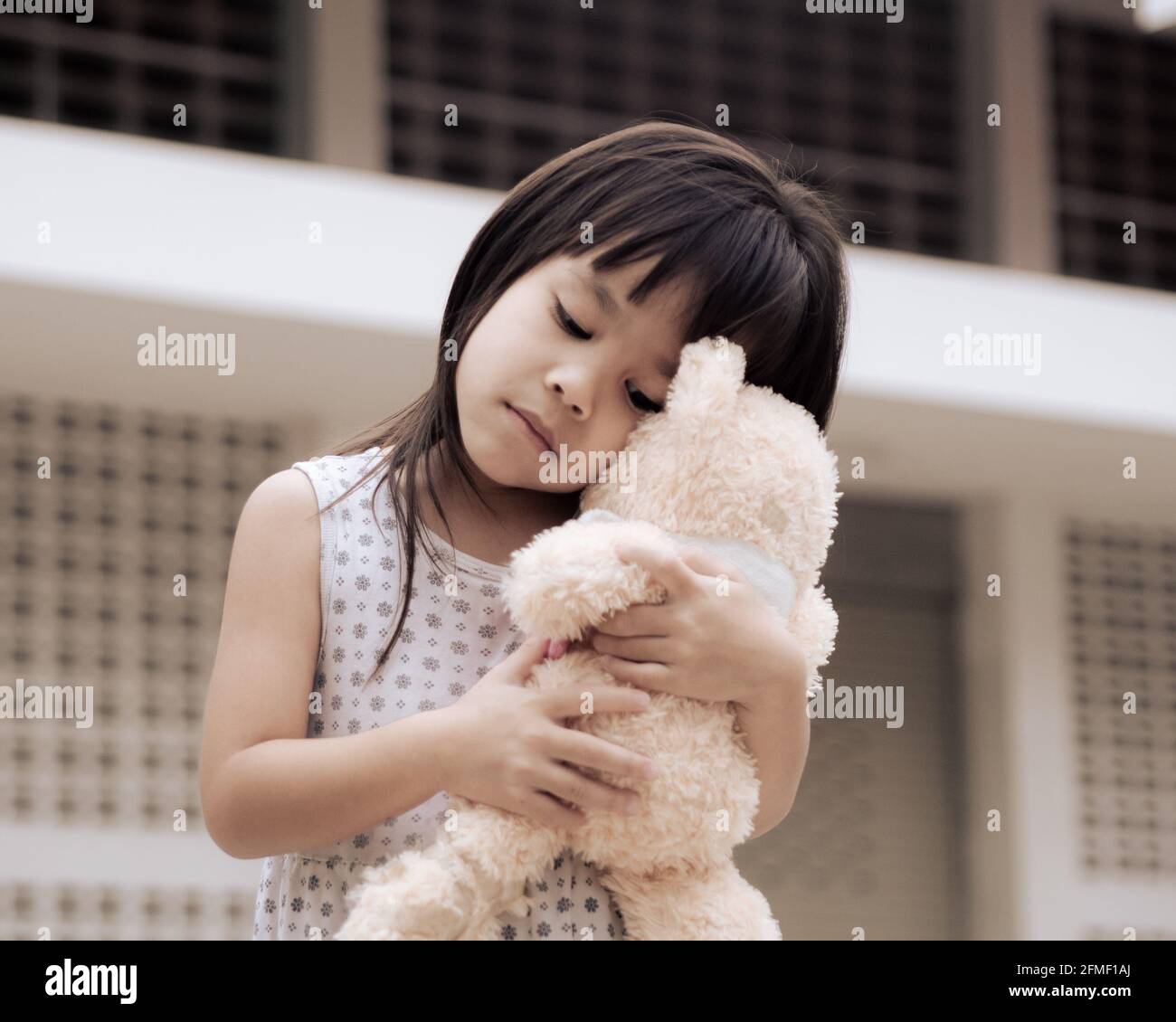 Sad little child girl hugging her teddy bear stands on home backyard. Stay at home to quarantine from coronavirus pandemic. Stock Photo