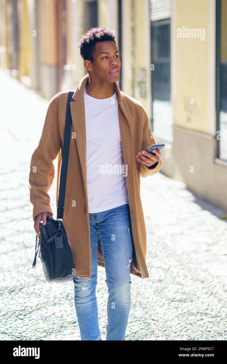 Young black man walking down the street carrying a briefcase and a smartphone. Stock Photo