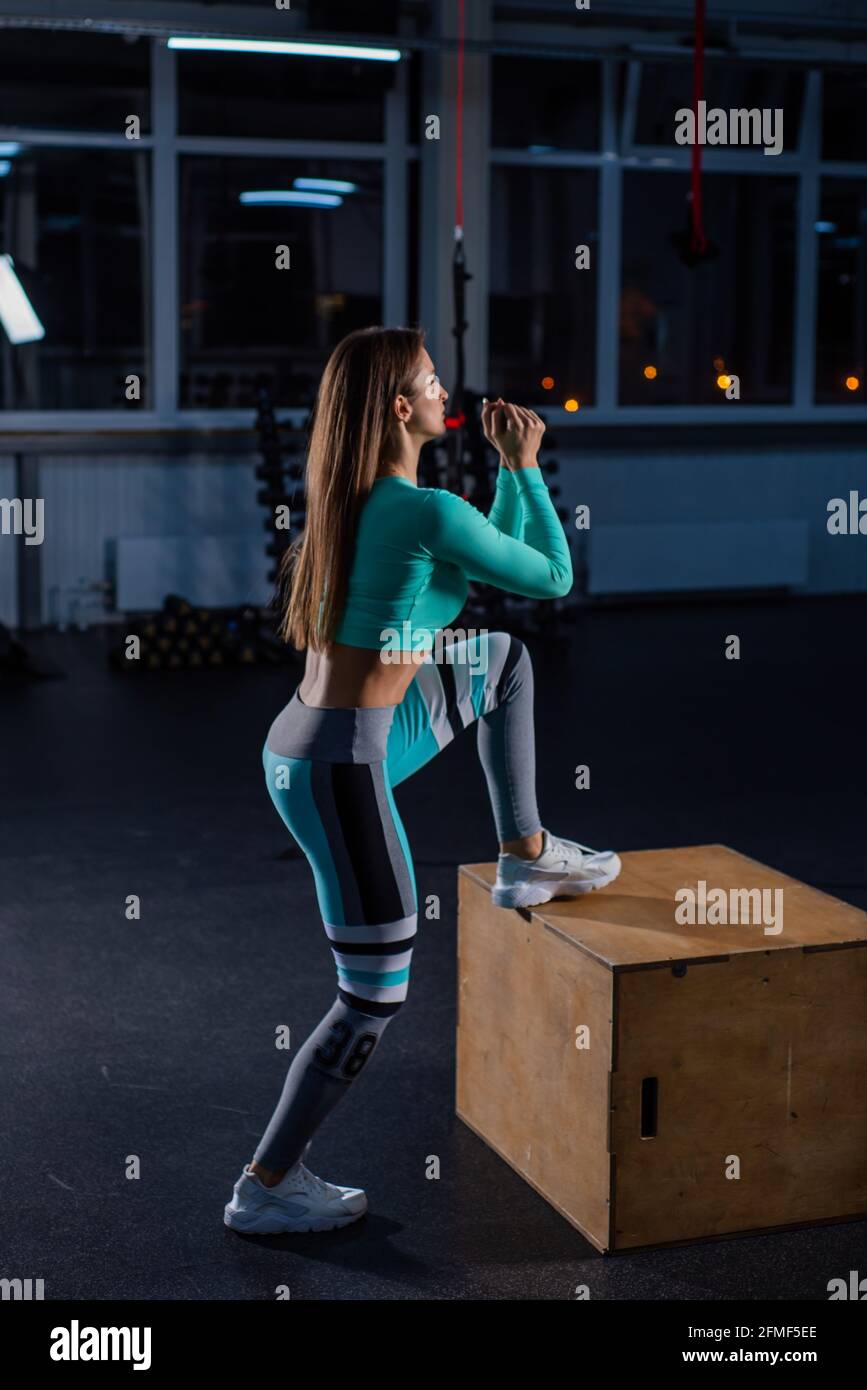 Fit young woman doing box jumping on dark background with copy space