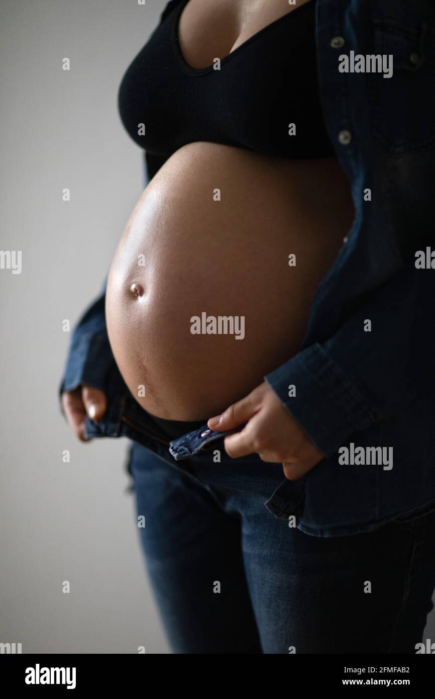 Pregnant woman touching her belly near the windows. Pregnancy and motherhood concept. Stock Photo