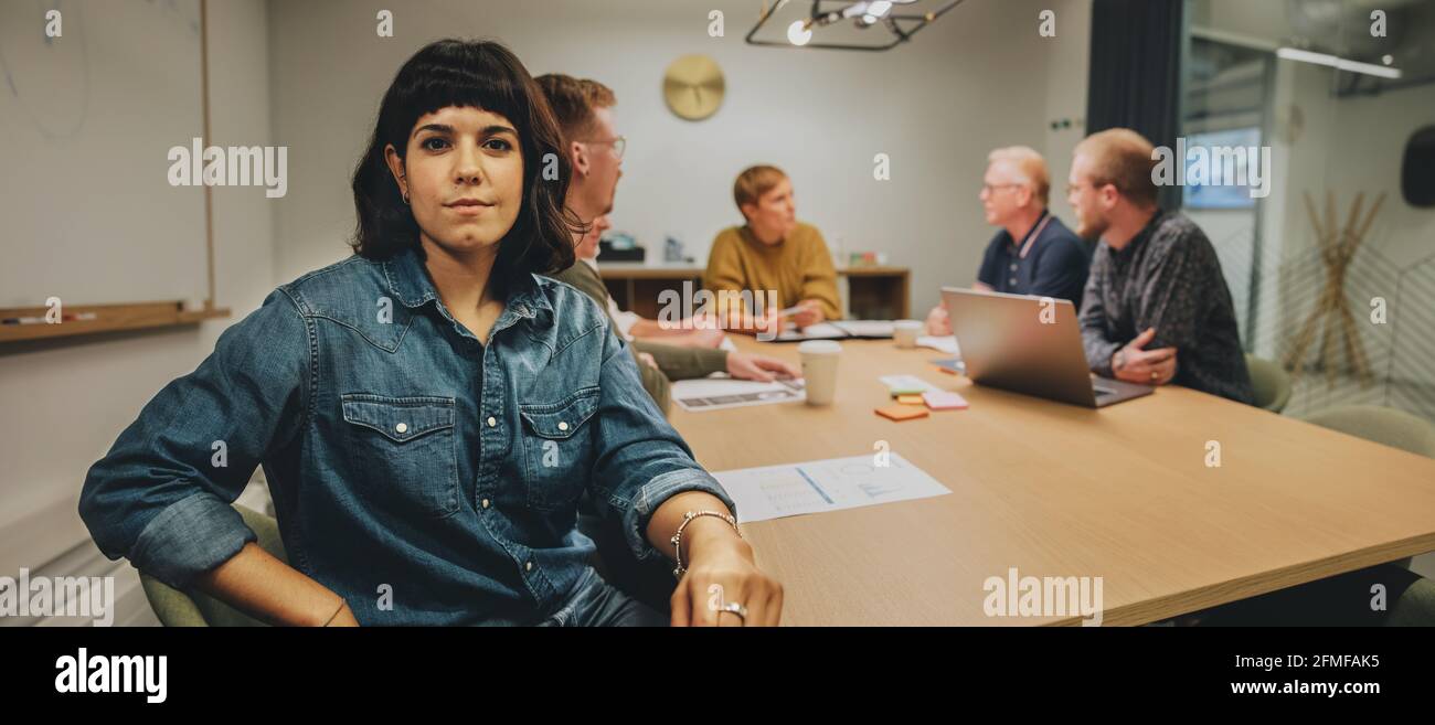 Portrait of a young woman sitting in meeting room with colleagues