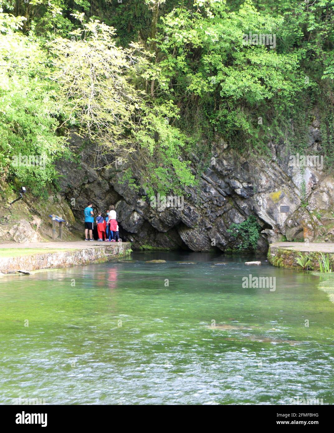 Cave entrance from which the source of the Ruente River flows a tributary of the River Saja Ruente Cantabria Spain with a family standing looking Stock Photo