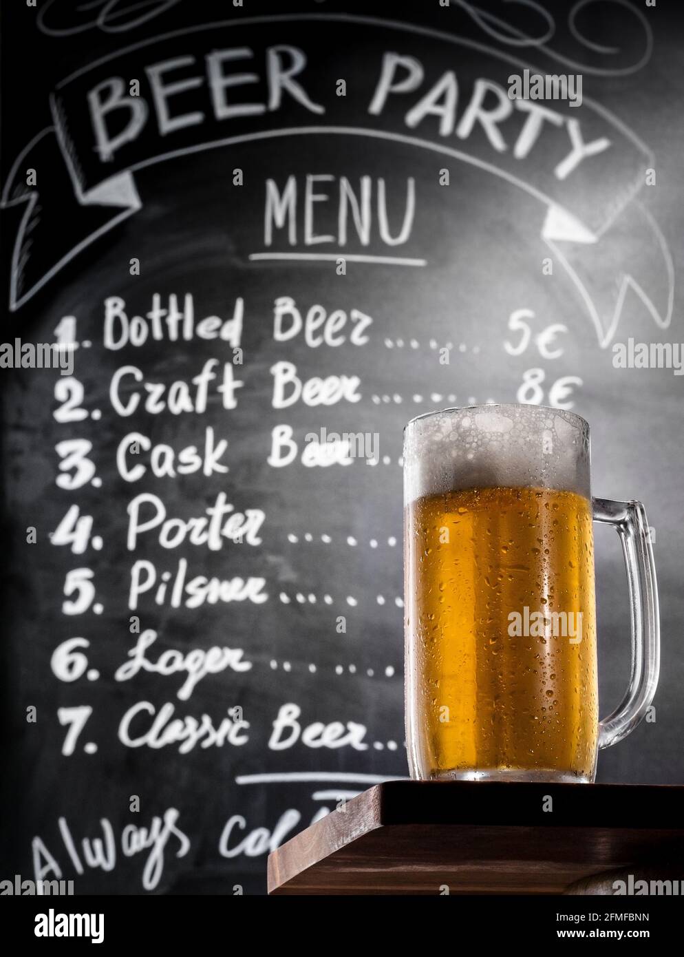 Full glass of the cold beer with foam on a wooden table at background of a chalk board with menu text, bottom-up view. Draft beer on a bar counter in Stock Photo