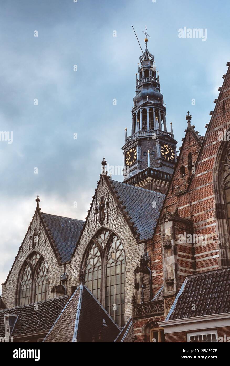 Gothic windows and tiles roofs of the Calvinist Oude Kerk church and old bell tower with clock at cloudy sky. Ancient christian architecture and churc Stock Photo